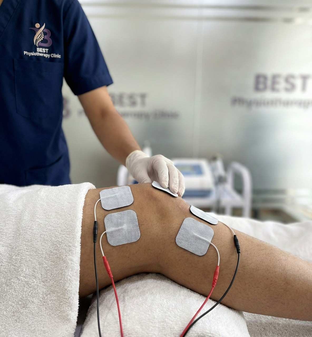 Physiotherapist placing interferential therapy pads on patient’s knee for treatment.